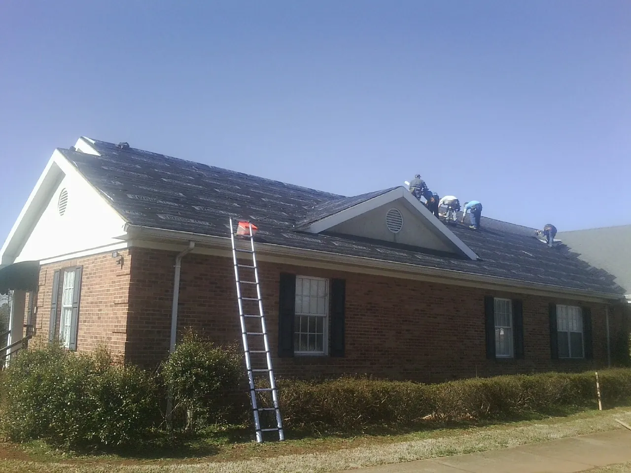 Crew tearing shingles off a brick ranch roof with a ladder set — Metal Roof Repair work by our crew in Skippack