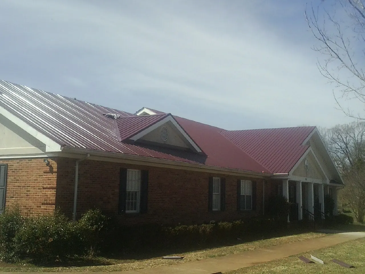 Red metal roof with gabled entries on a long brick building, from a Hail Damage Roof Repair job in Skippack