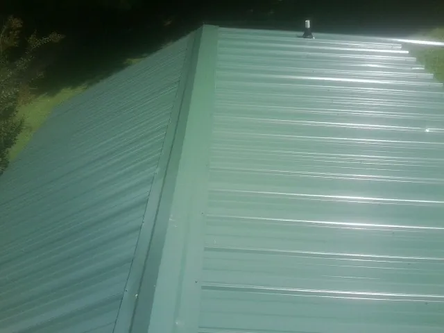 New green metal panels meeting at the ridge of a roof — Flat Roof Repair work by our crew in Skippack