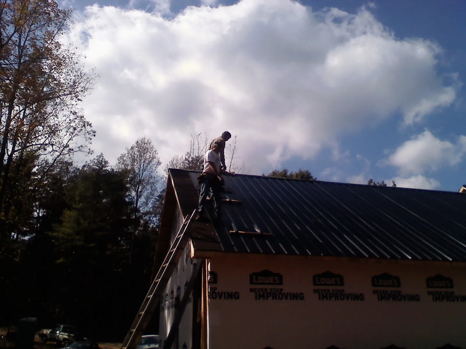 Roofer fastening dark metal panels high against a cloudy sky, from a Roof Inspection job in Skippack