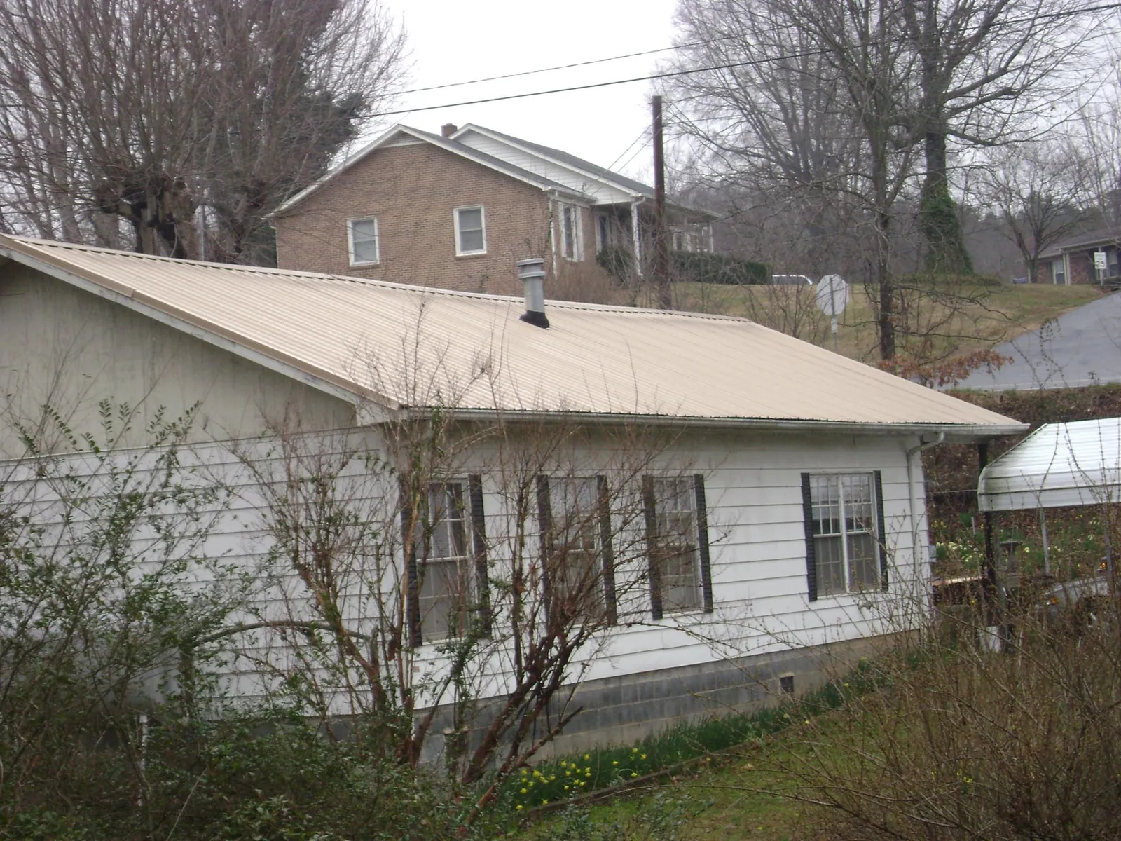 Tan metal roof on a white sided house set into a hillside — Commercial Roofing by Roofing Brothers in Skippack